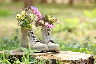 Photo of Beautiful flowers in boots on stump outdoors, space for text