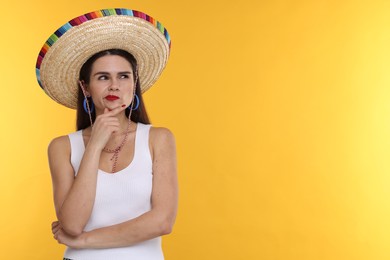 Photo of Thoughtful woman in Mexican sombrero hat on yellow background. Space for text