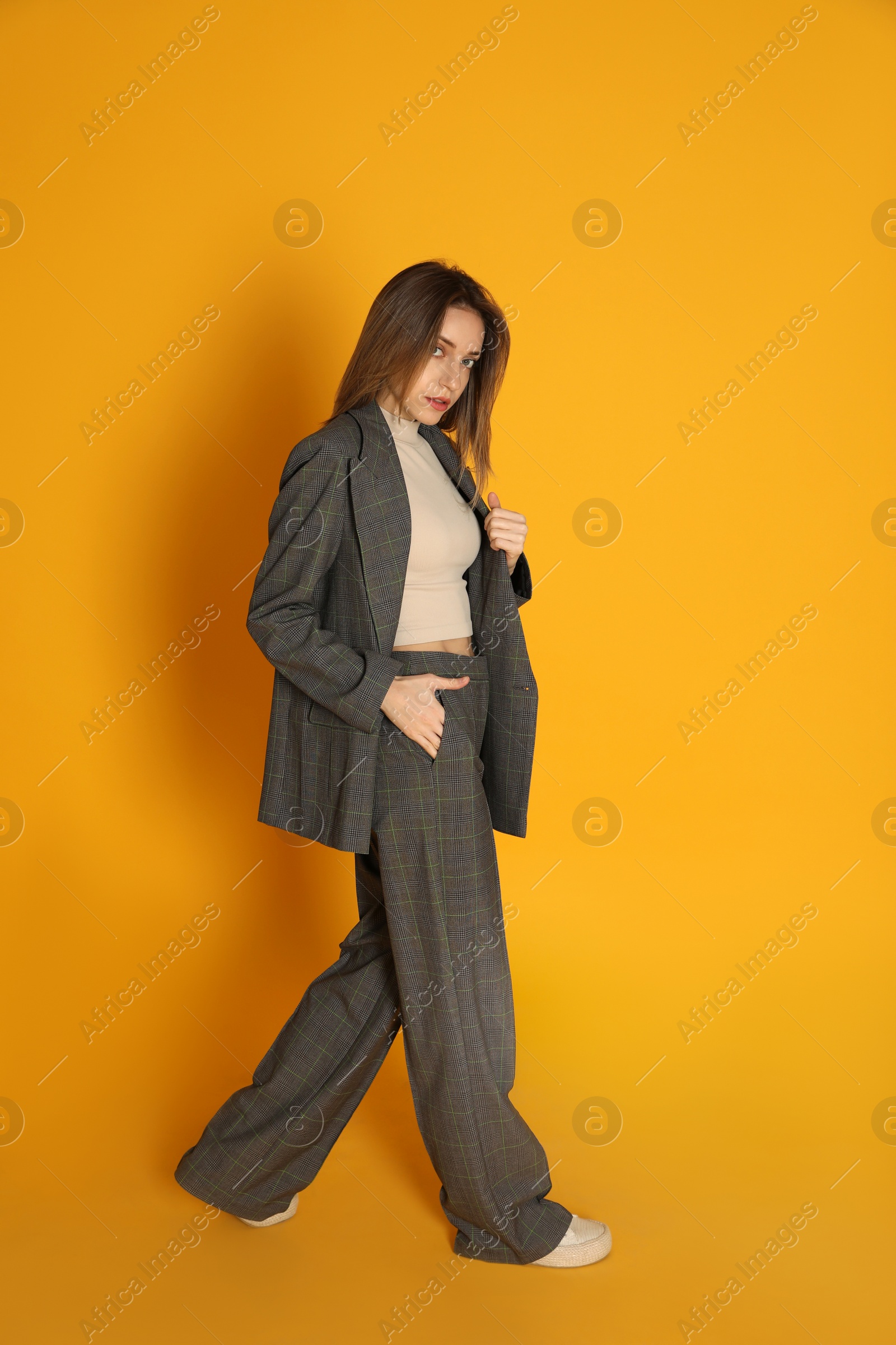 Photo of Full length portrait of beautiful young woman in fashionable suit on yellow background. Business attire