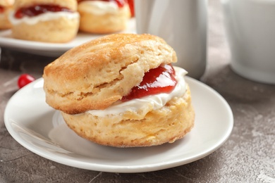 Tasty scone with clotted cream and jam on plate, closeup