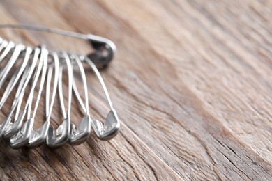 Many safety pins on wooden table, closeup. Space for text