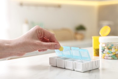 Photo of Woman with pills and organizer at white marble table, closeup