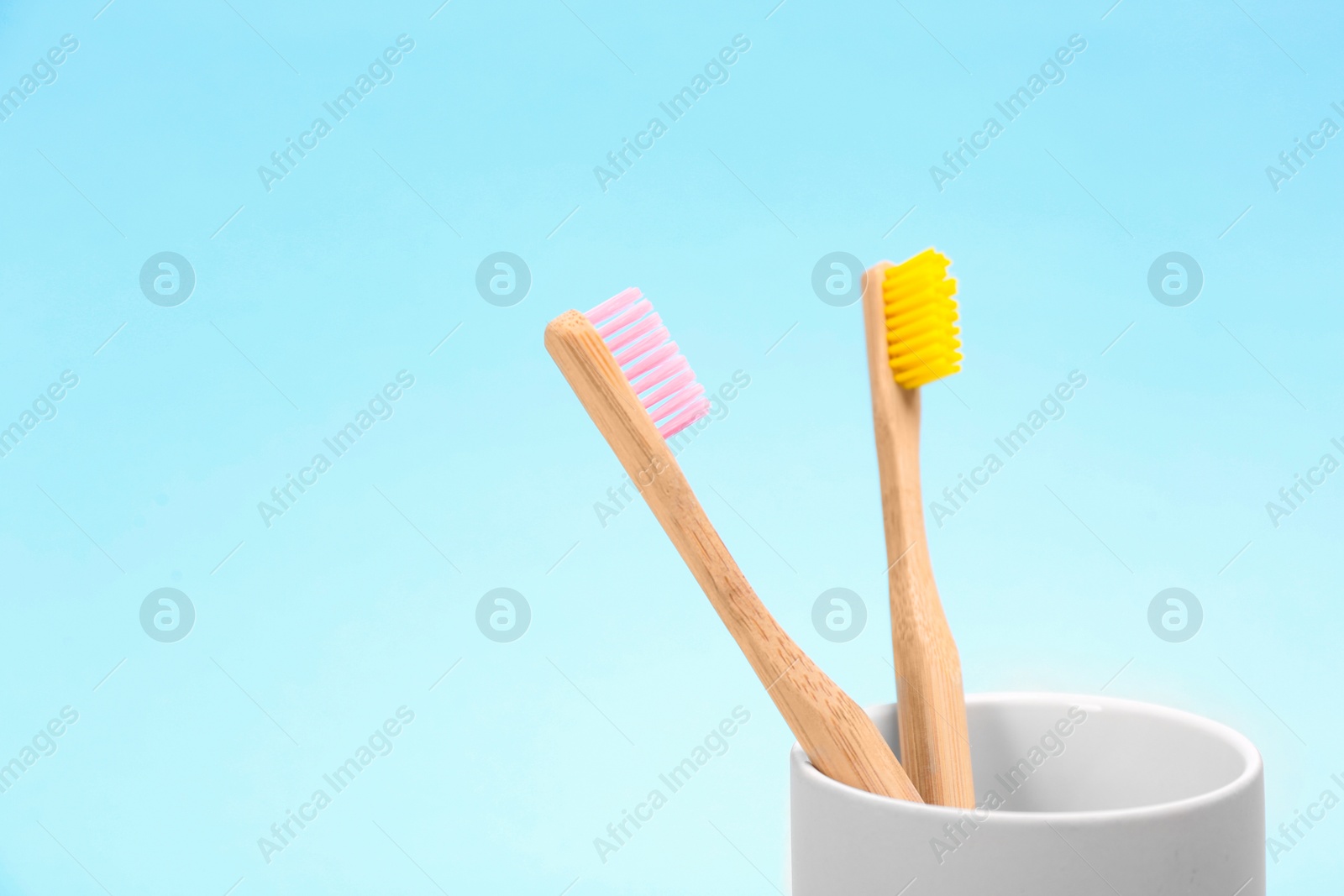 Photo of Toothbrushes made of bamboo in holder on light blue background. Space for text