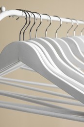 Photo of White clothes hangers on metal rail against beige background, closeup
