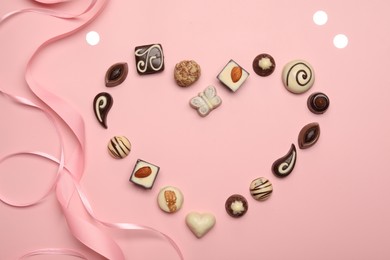 Heart made with delicious chocolate candies on light pink background, flat lay