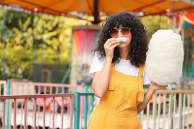 Photo of Beautiful woman having fun with cotton candy at funfair. Space for text