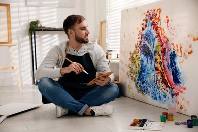 Photo of Young man painting on canvas with brush in artist studio