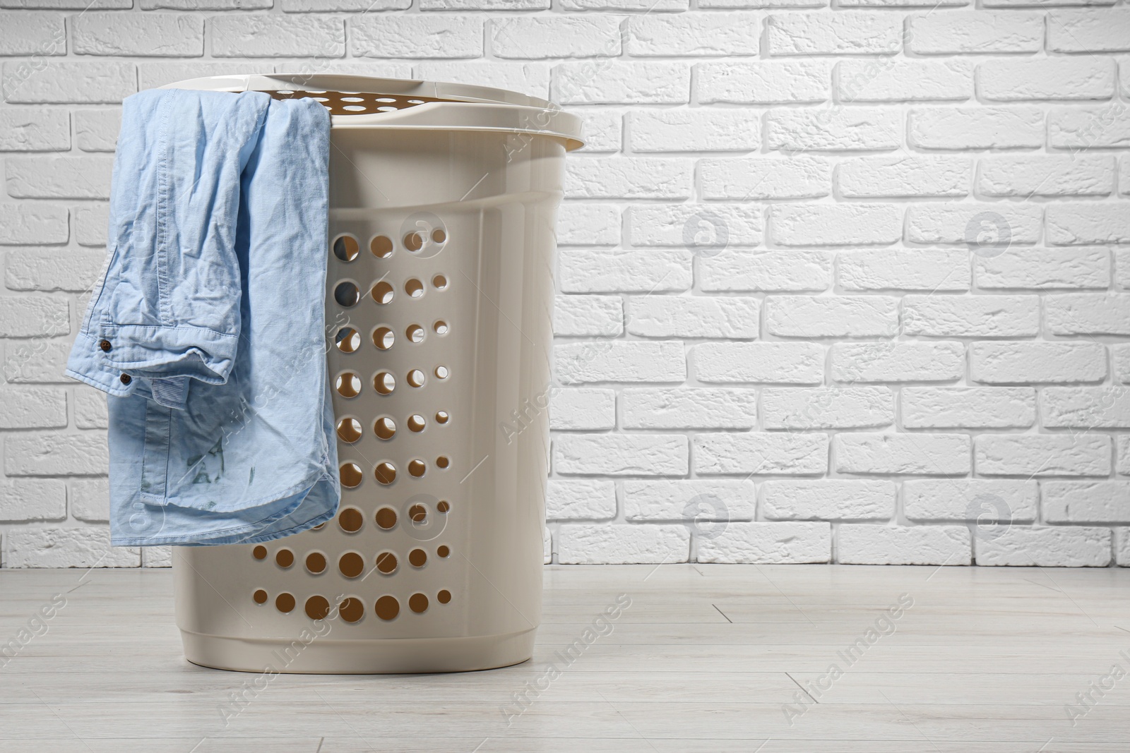 Photo of Laundry basket with clothes near white brick wall. Space for text