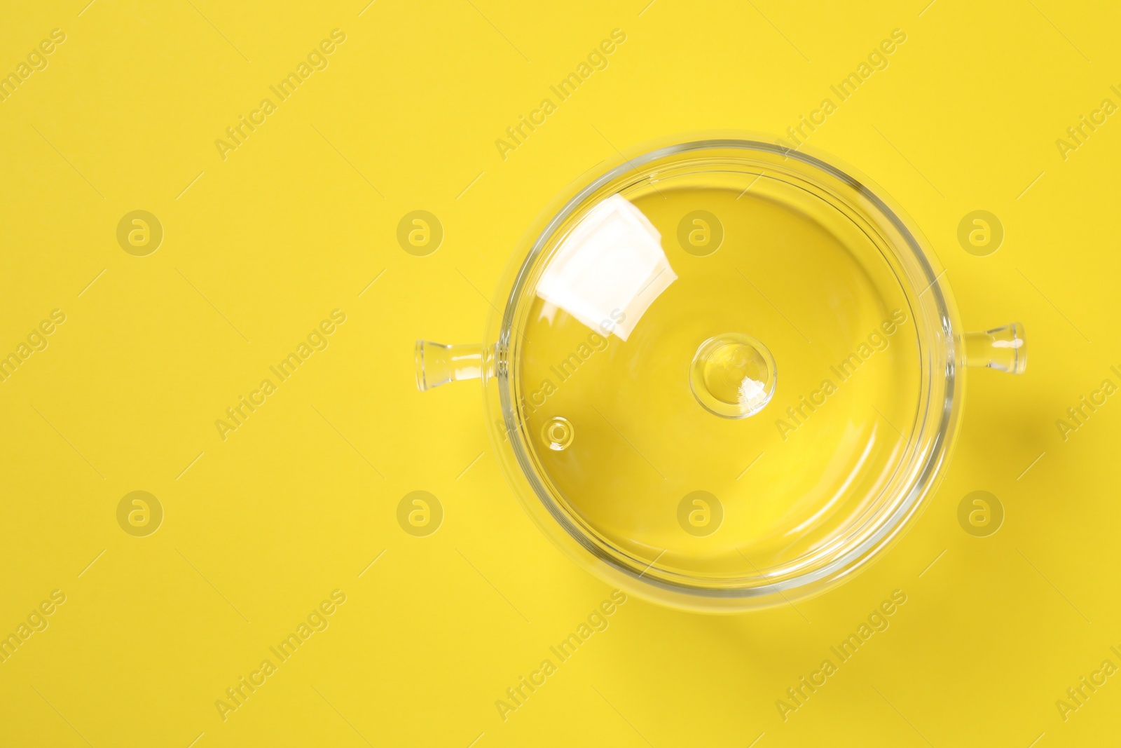 Photo of Glass pot with lid on yellow background, top view. Space for text