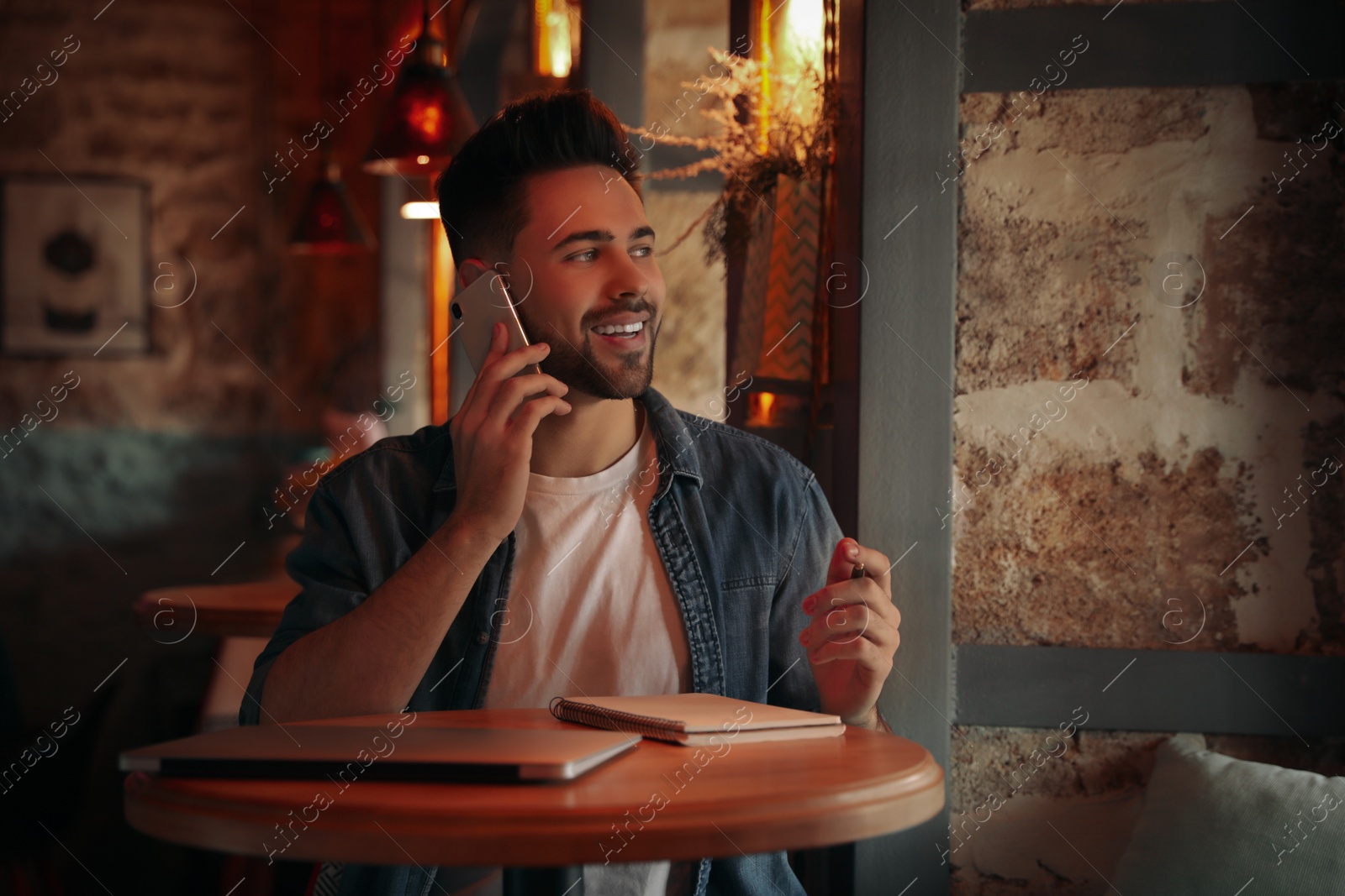 Photo of Young blogger talking on phone at table in cafe