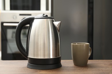 Photo of Modern electric kettle and cup on table in kitchen. Space for text