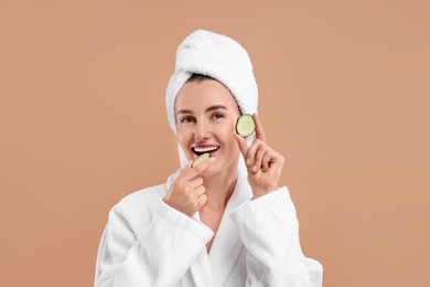 Beautiful woman in bathrobe with pieces of cucumber on beige background