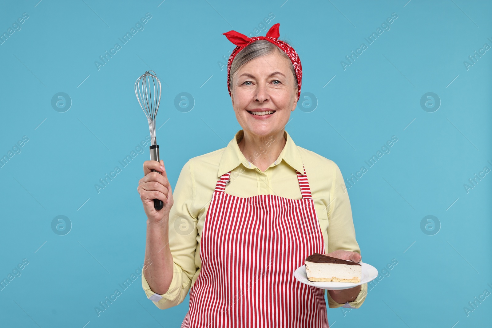 Photo of Happy housewife with whisk and piece of cake on light blue background