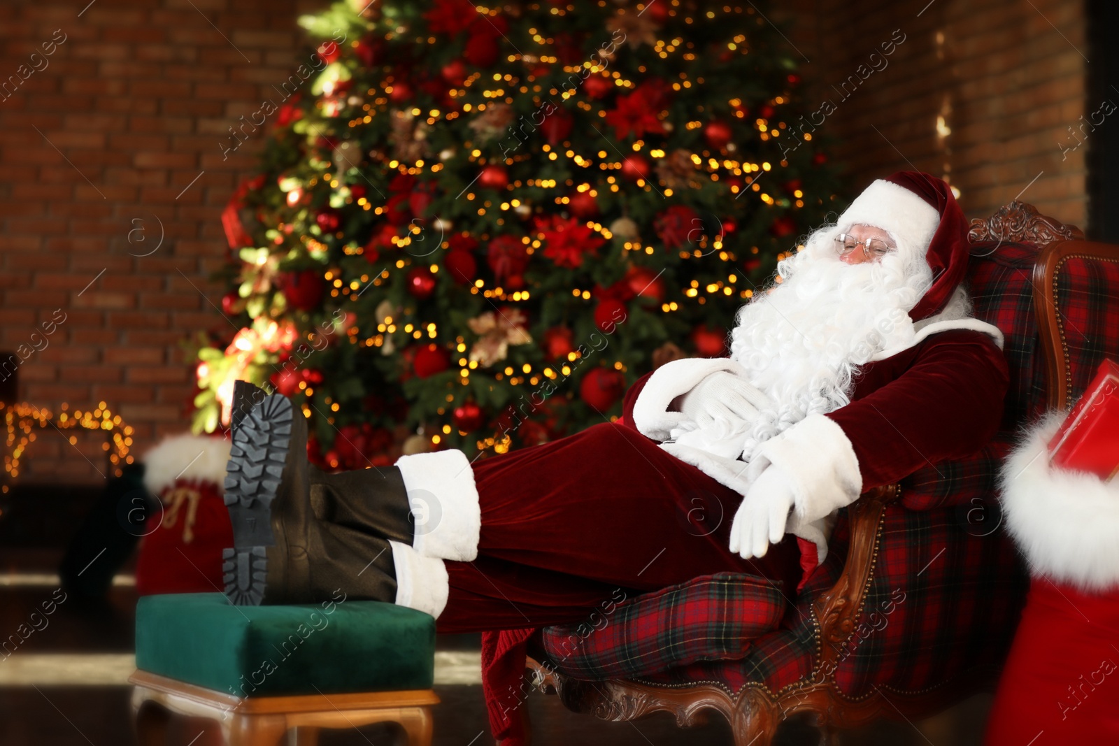 Photo of Santa Claus resting in armchair near decorated Christmas tree indoors