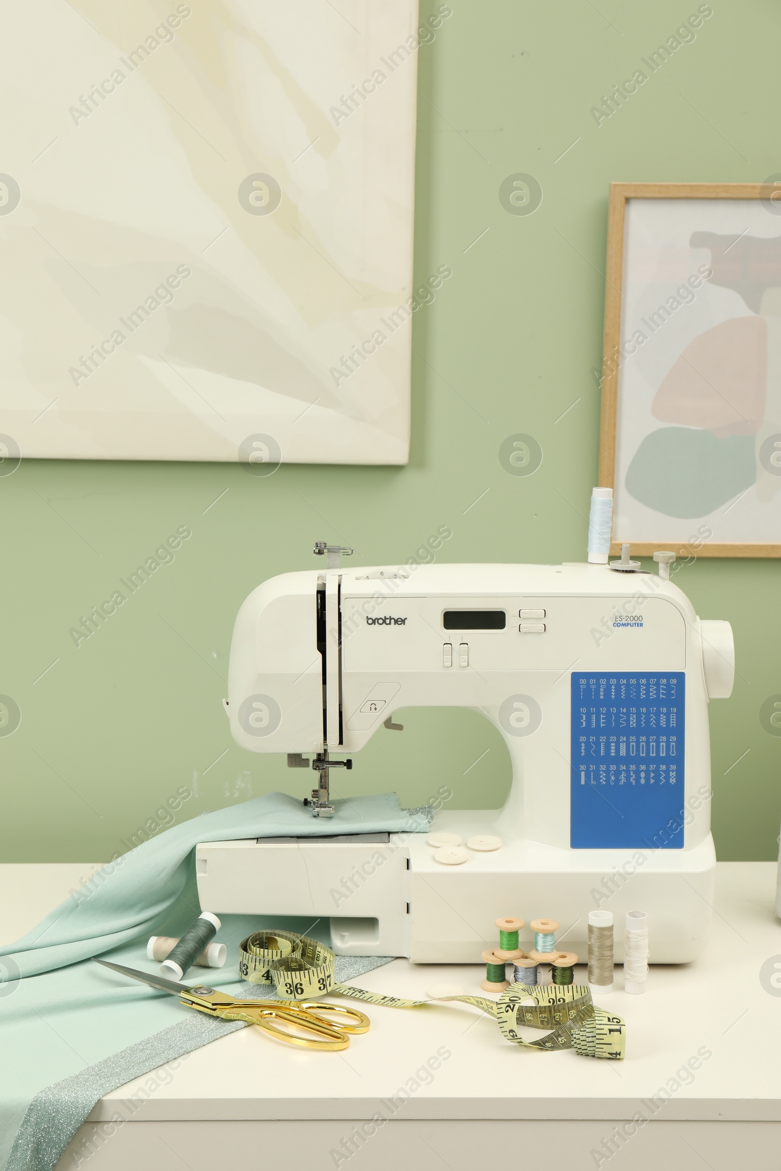 Photo of Modern sewing machine with cloth and craft accessories on white table near light green wall