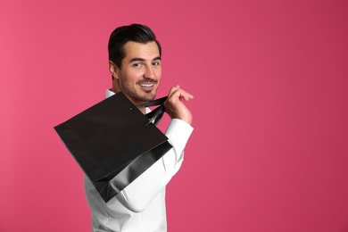 Young handsome man holding black paper bag on pink background. Mockup for design