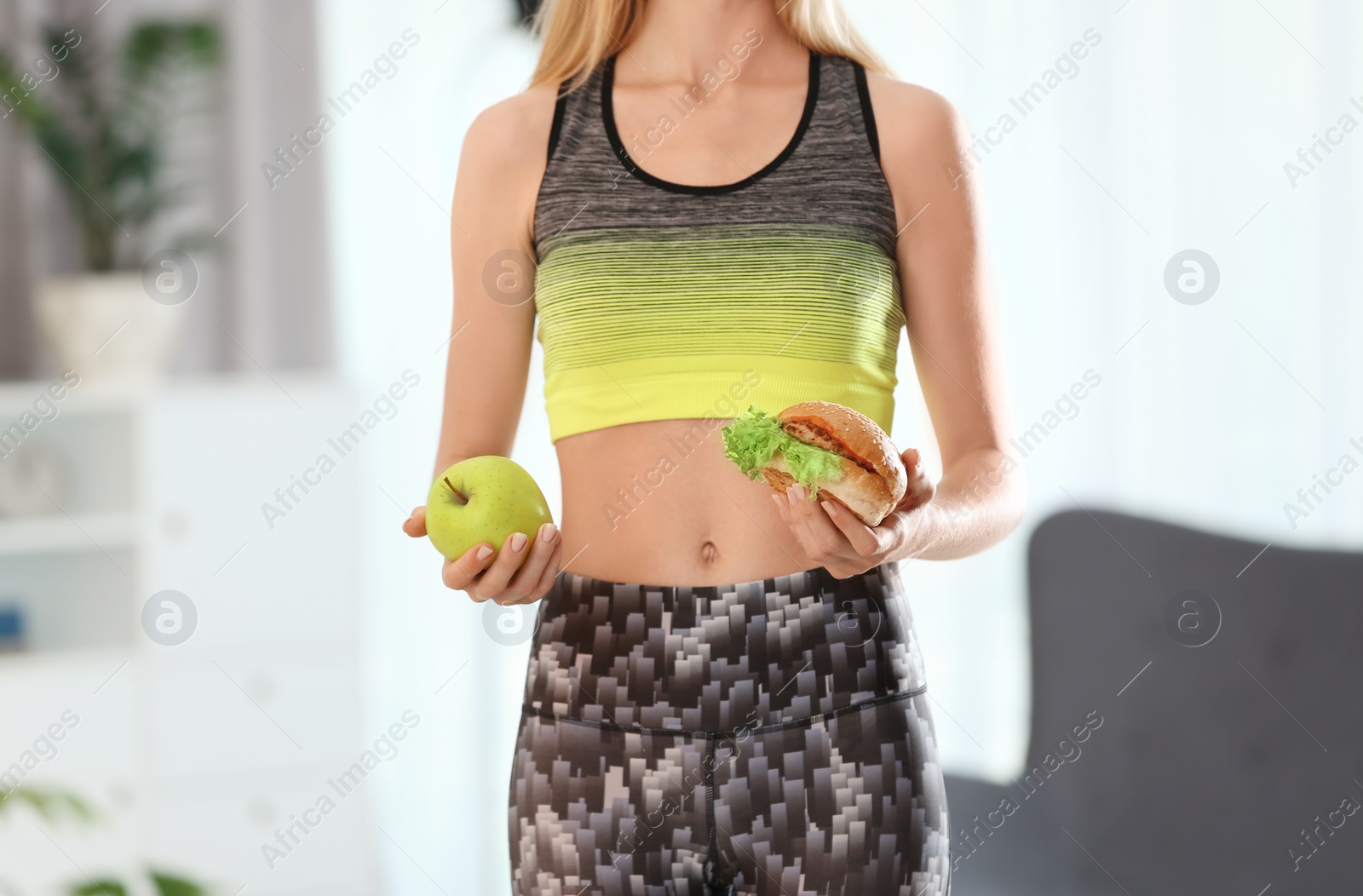 Photo of Woman holding tasty sandwich and fresh apple, indoors. Choice between diet and unhealthy food