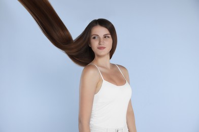 Photo of Young woman with strong healthy hair on light blue background