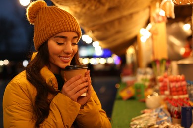 Young woman with cup of hot drink spending time at Christmas fair, space for text