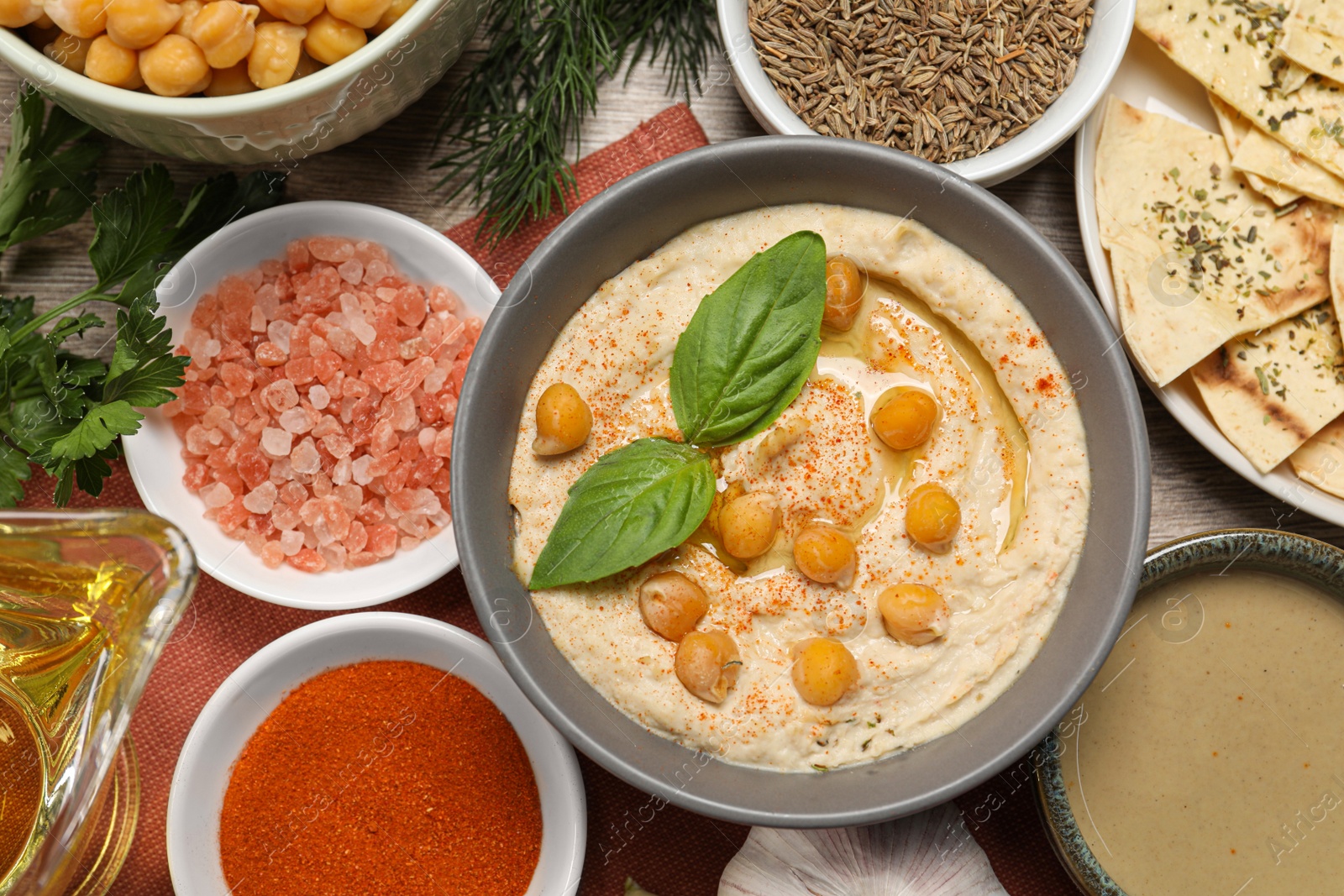 Photo of Delicious creamy hummus with chickpeas and different ingredients on wooden table, flat lay