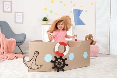Cute little girl playing with cardboard ship at home