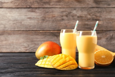 Tasty tropical drink with mango and fresh fruits on wooden table. Space for text