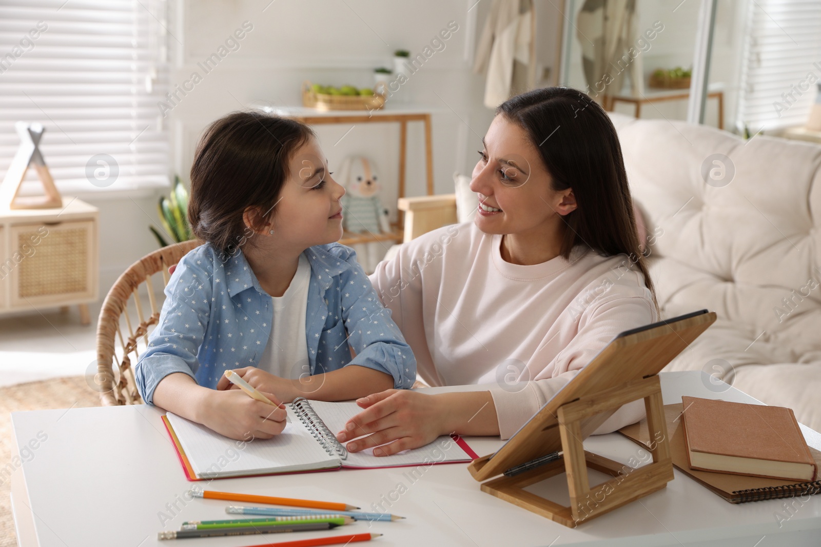 Photo of Mother helping her daughter with homework using tablet at home