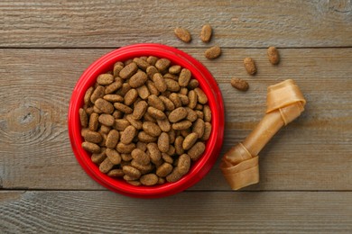 Photo of Dry dog food and treat (chew bone) on wooden floor, flat lay