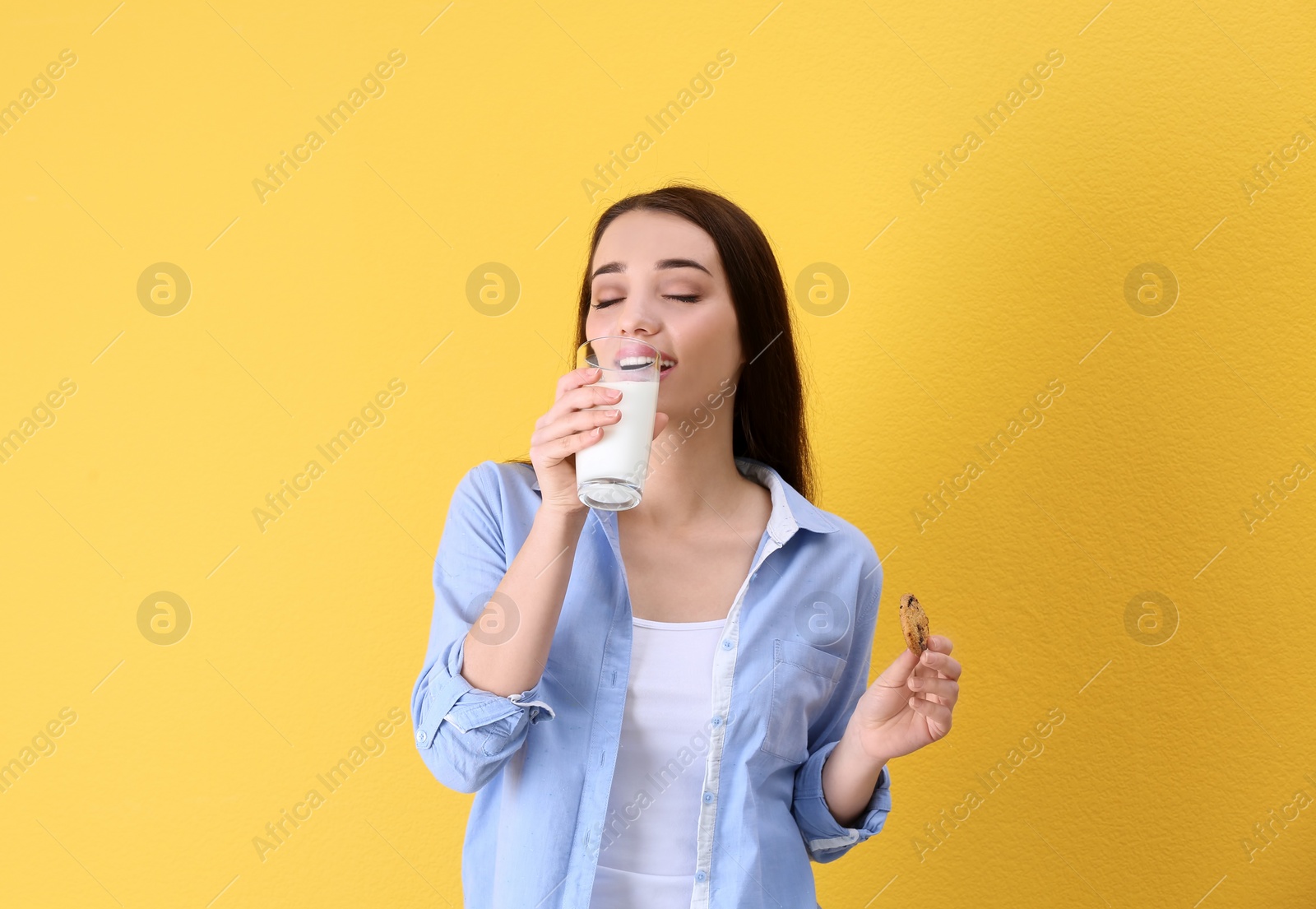 Photo of Beautiful young woman drinking milk with cookie on color background