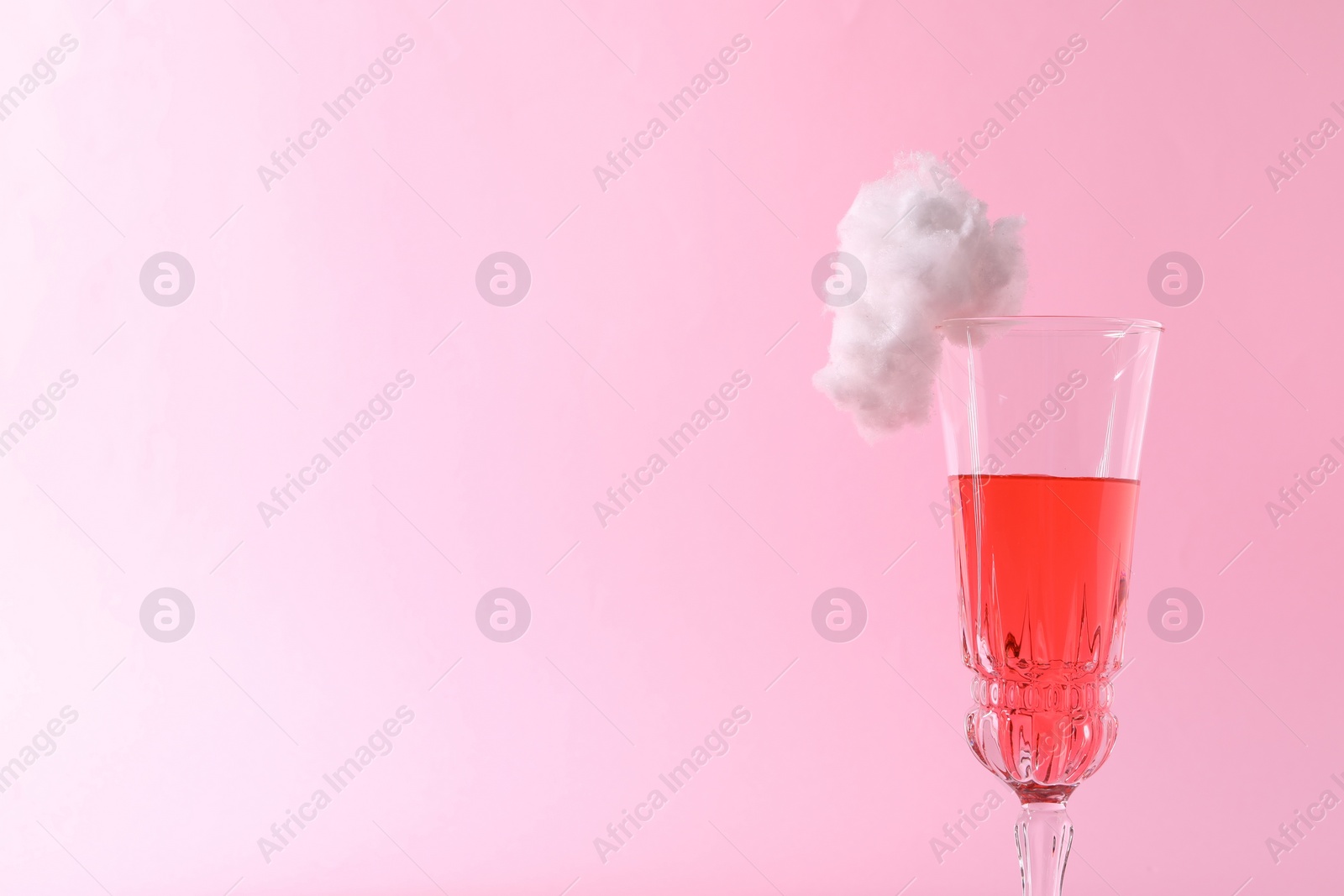 Photo of Tasty cocktail in glass decorated with cotton candy on pink background, closeup. Space for text