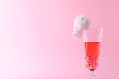 Photo of Tasty cocktail in glass decorated with cotton candy on pink background, closeup. Space for text