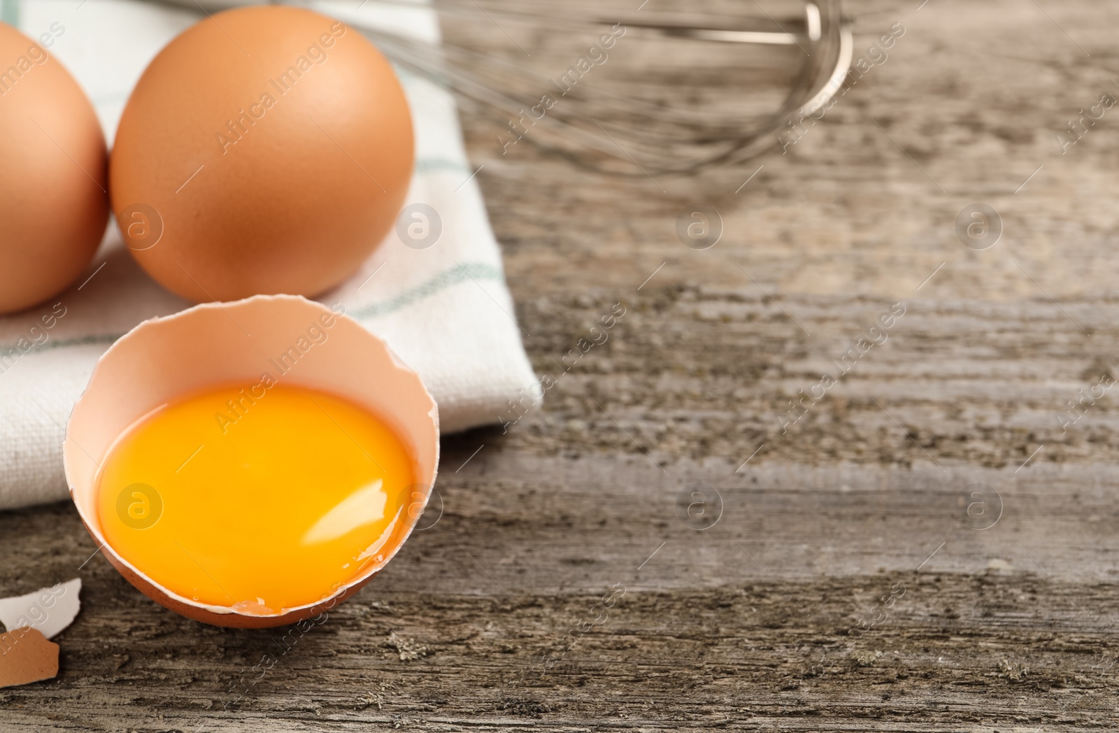 Photo of Raw chicken eggs and shell with yolk on wooden table, closeup. Space for text