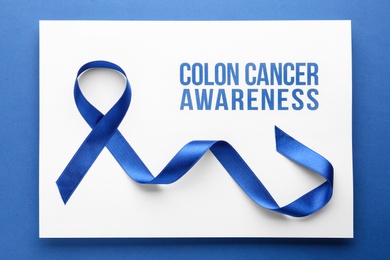 Photo of Card with words COLON CANCER AWARENESS and blue ribbon on color background, top view