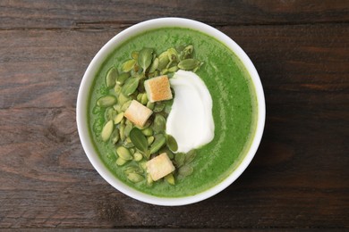 Photo of Delicious broccoli cream soup with croutons, sour cream and pumpkin seeds on wooden table, top view