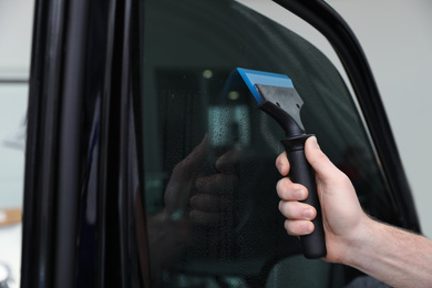 Worker washing tinted car window in workshop, closeup