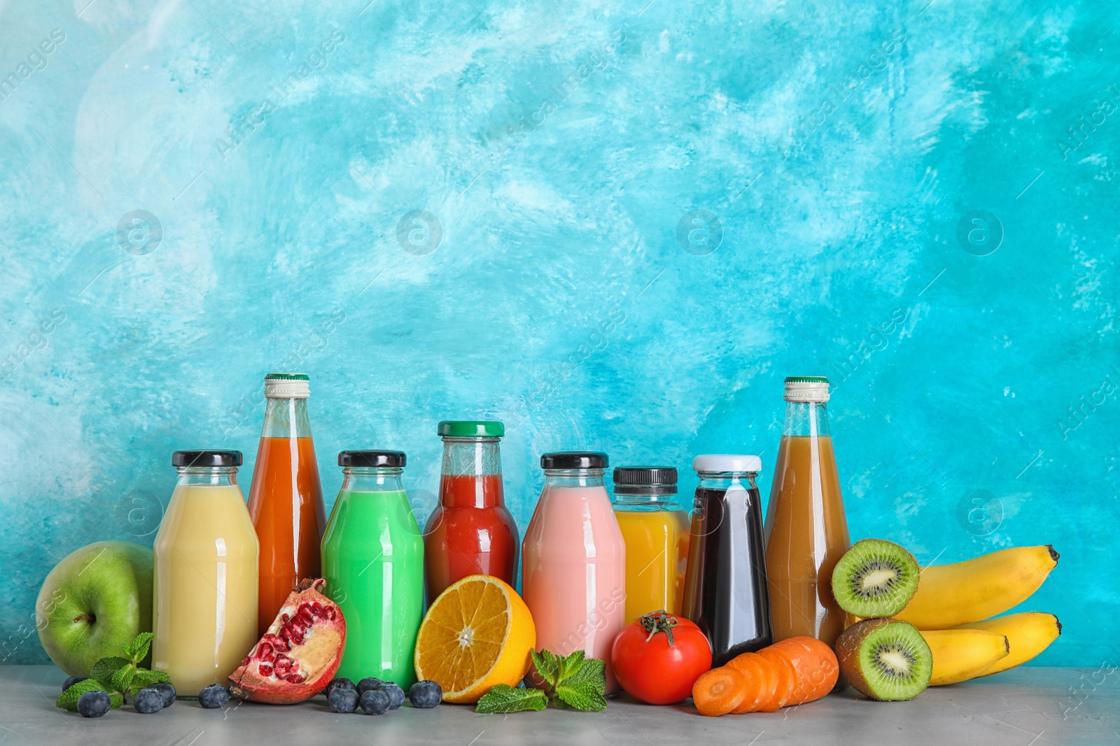 Photo of Bottles with different drinks and ingredients on table against color background