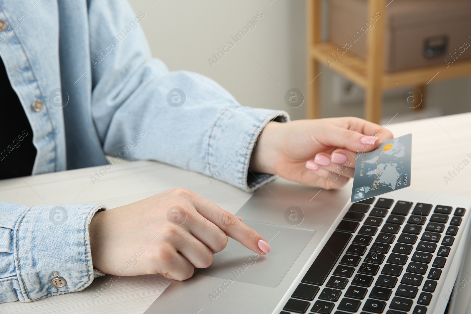 Photo of Online payment. Woman with credit card using laptop at white wooden table indoors, closeup