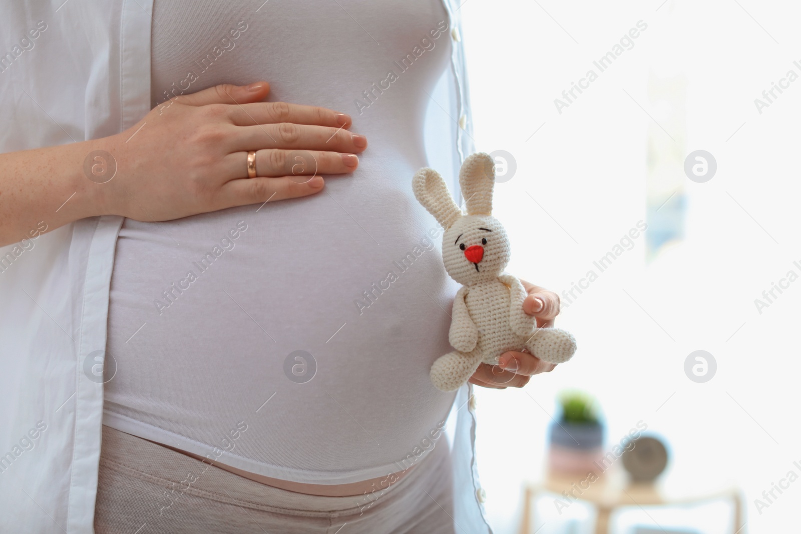 Photo of Pregnant woman holding toy near tummy in light room at home, closeup