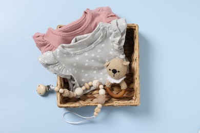 Photo of Different baby accessories and clothes in wicker box on light blue background, top view