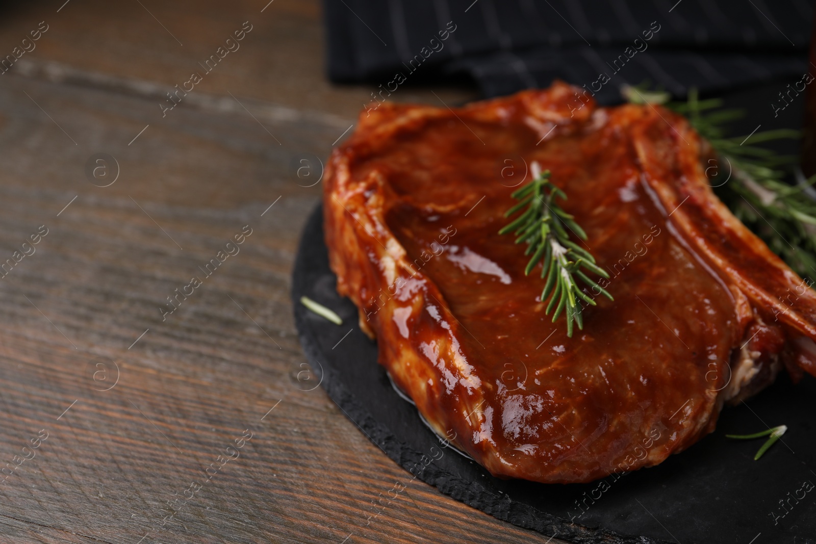 Photo of Tasty marinated meat and rosemary on wooden table, closeup. Space for text