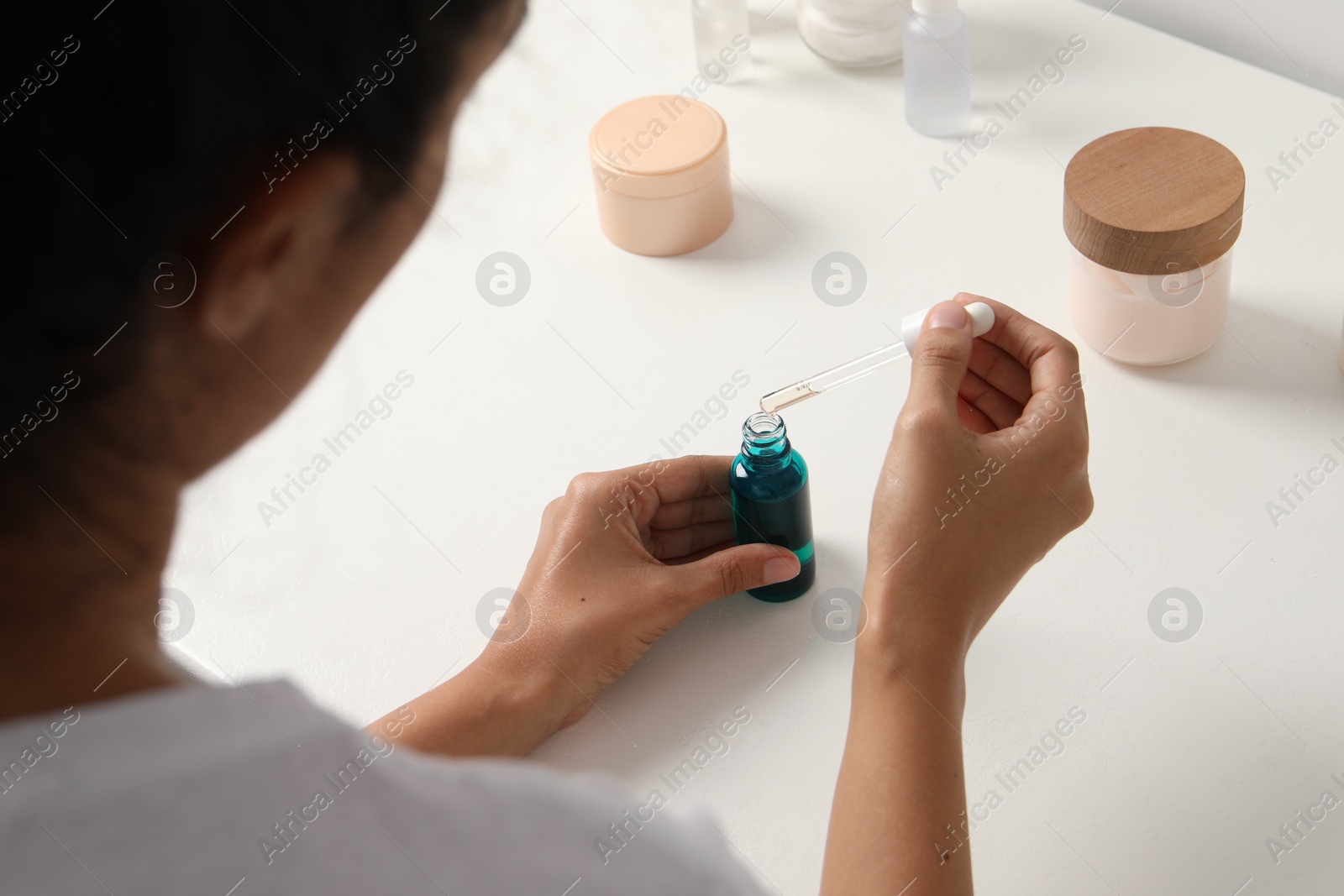 Photo of Woman with bottle of cosmetic serum at white table, closeup