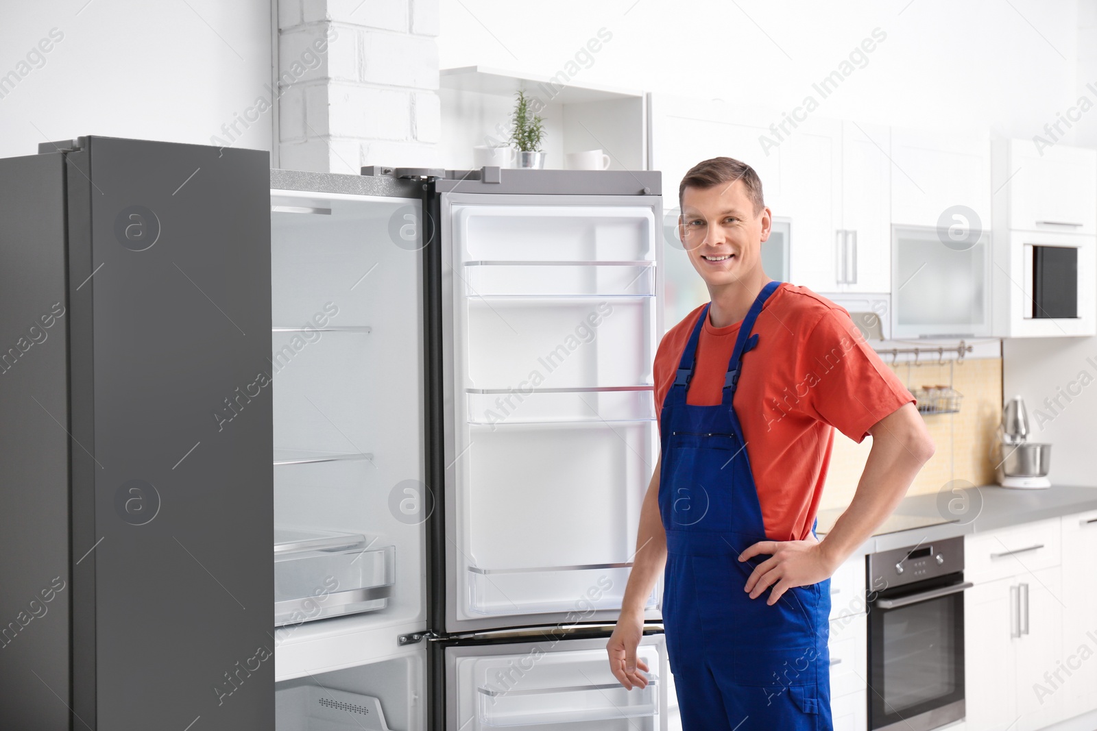 Photo of Male technician in uniform near refrigerator indoors