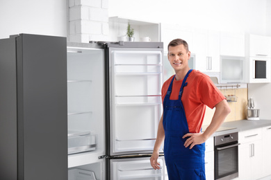 Photo of Male technician in uniform near refrigerator indoors