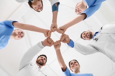 Photo of Team of medical doctors putting hands together indoors, bottom view