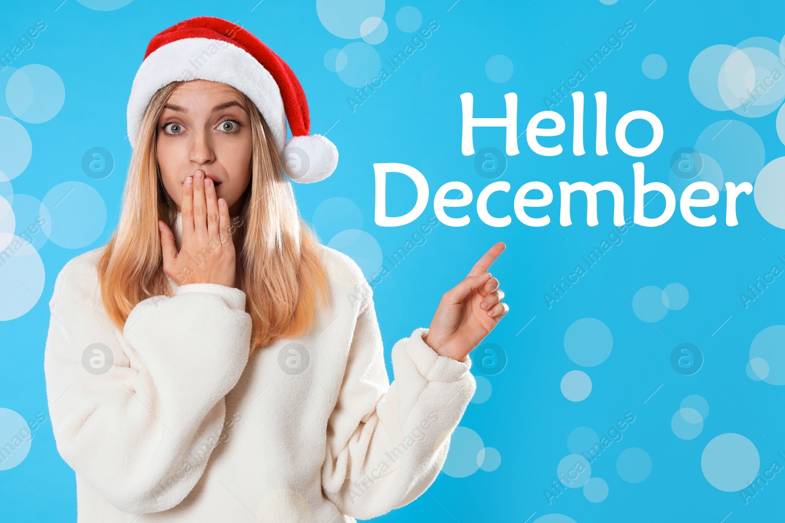 Image of Hello December greeting card. Surprised woman in Santa hat on light blue background, bokeh effect