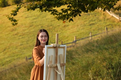 Photo of Beautiful young woman drawing on canvas in nature