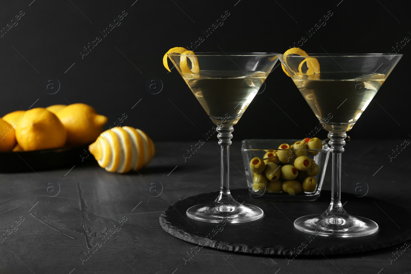 Photo of Glasses of Lemon Drop Martini cocktail with zest on grey table against black background. Space for text