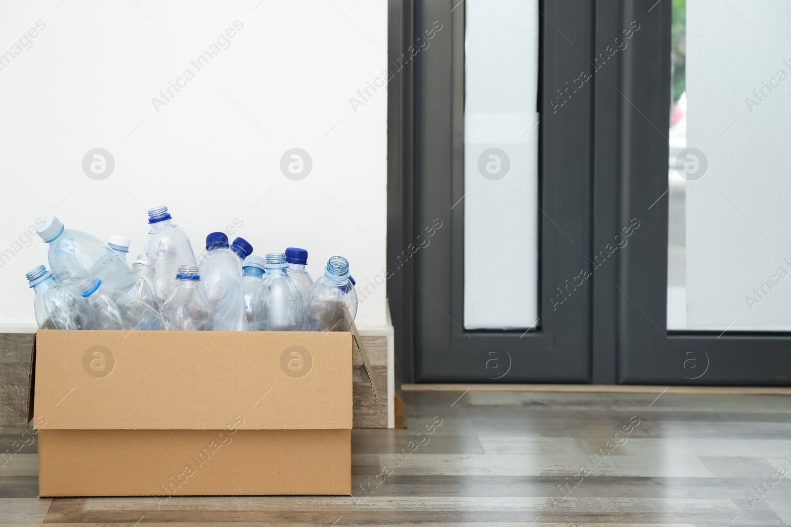 Photo of Cardboard box with used plastic bottles near entrance door in hallway. Recycling problem