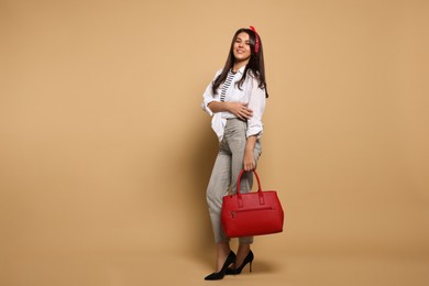 Young woman with stylish bag on beige background