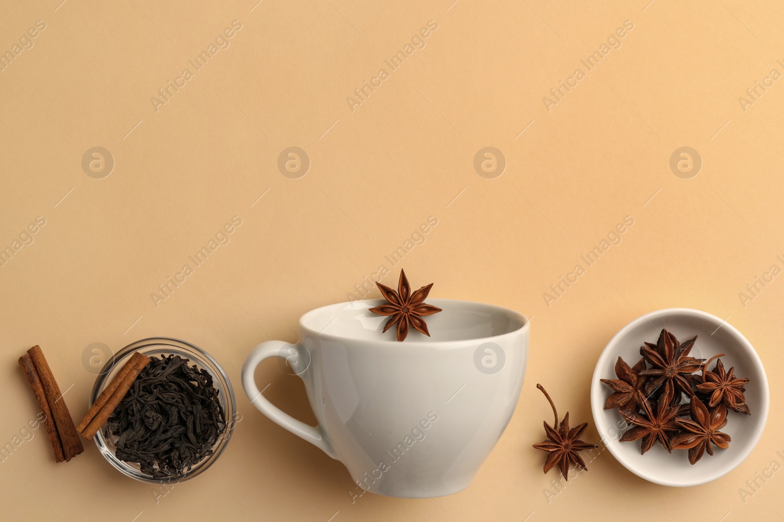 Photo of Cup with anise stars, dry tea and cinnamon sticks on beige background, flat lay. Space for text